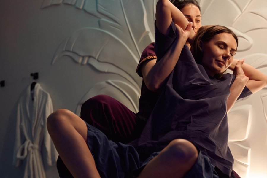 a woman sitting on a bed with another woman holding her back