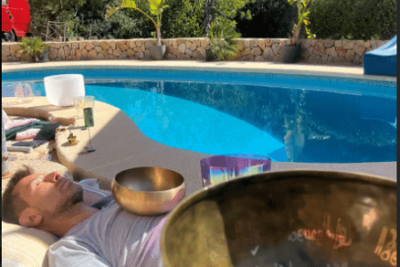 A man laying by a pool meditating with a singing bow resting on his chest.