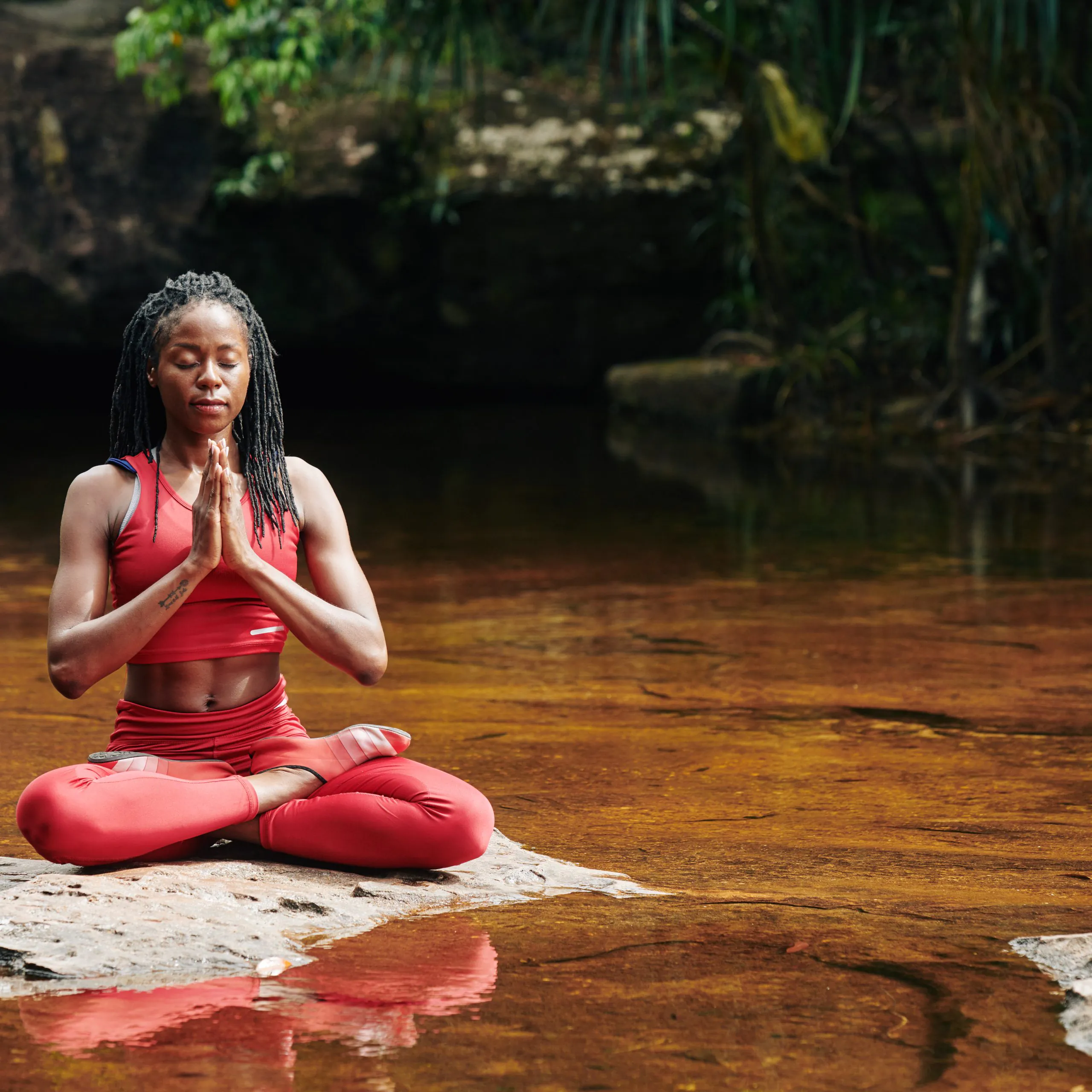 a woman sitting on a rock in the water with her hands together